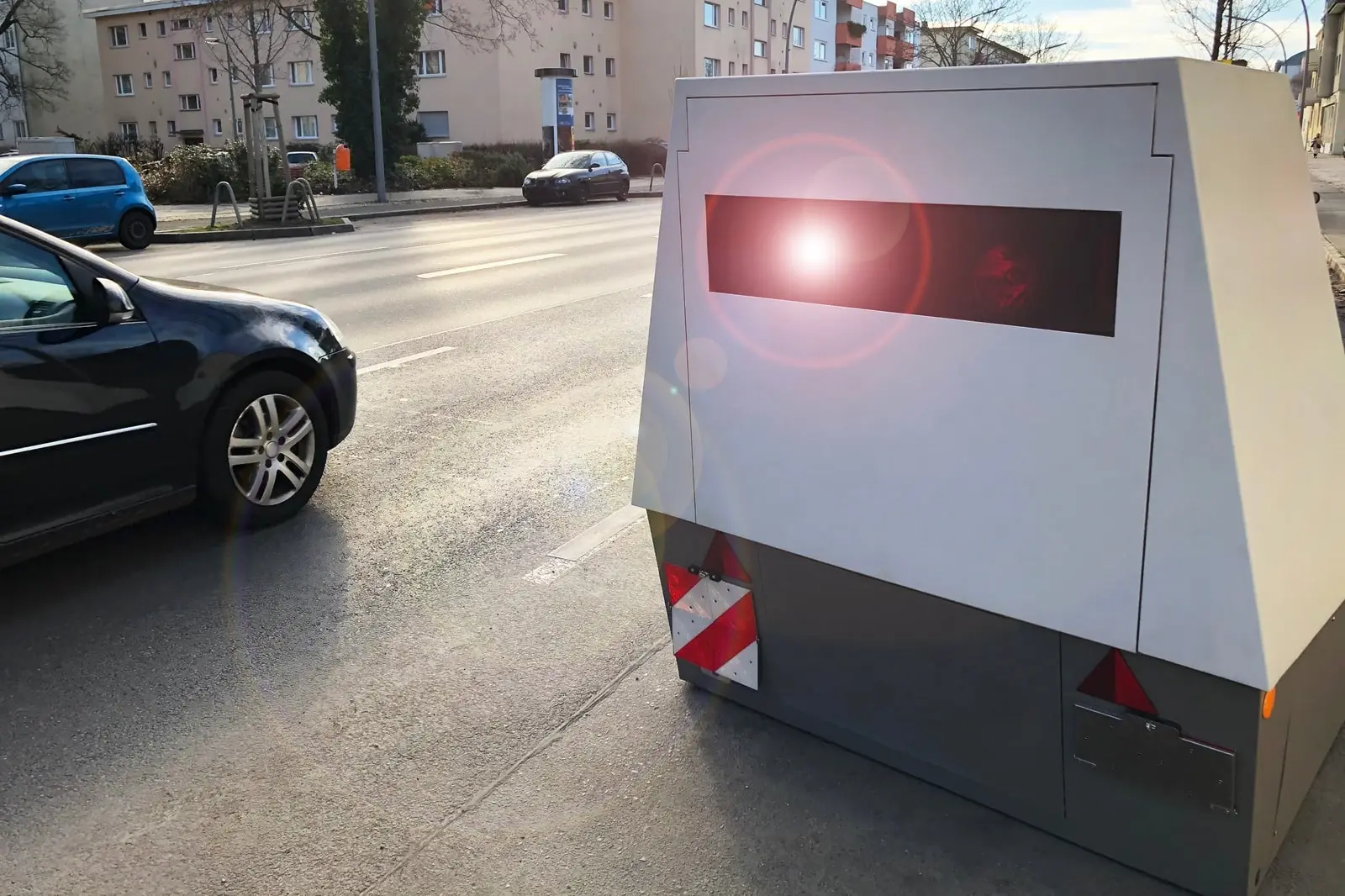 Ein Auto wird innerorts von einem Laserblitzer geblitzt und das rote Licht leuchtet leicht auf